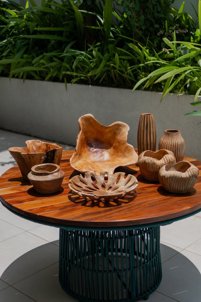 Wooden bowls and vases on a patio table with lush green plants in the background.