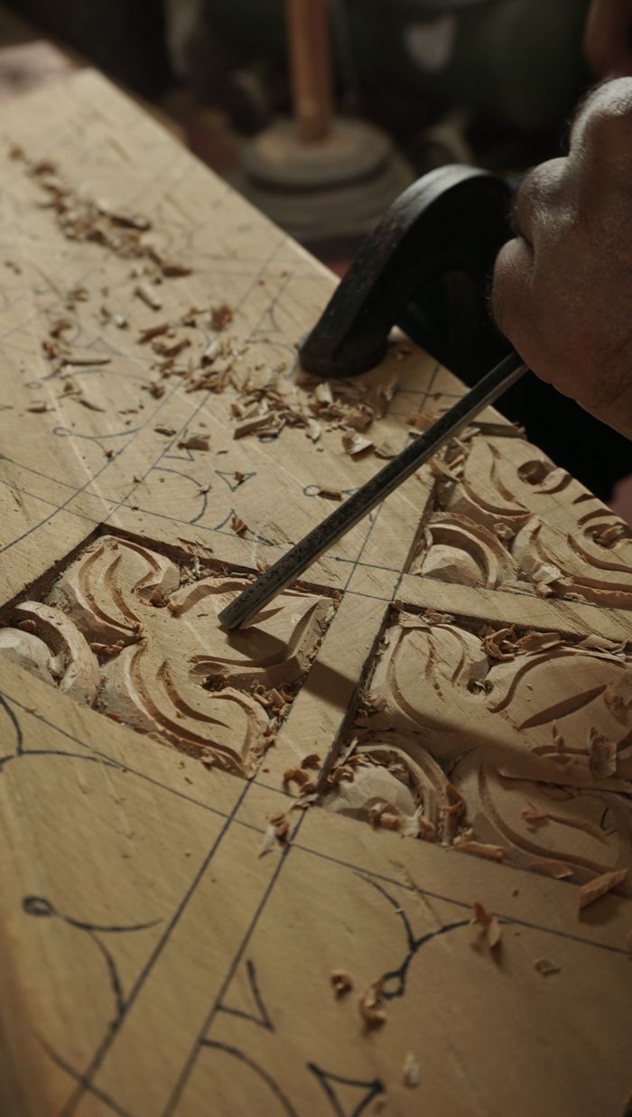 Close-up of hand carving intricate designs on wood using chisels in Bengaluru workshop.