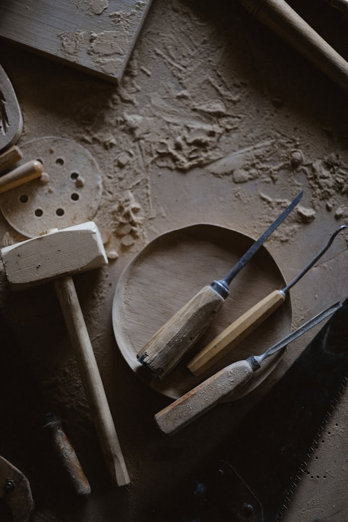 Top view of joinery mallet and set of chisels on wooden board placed on messy workbench with shavings in carpentry